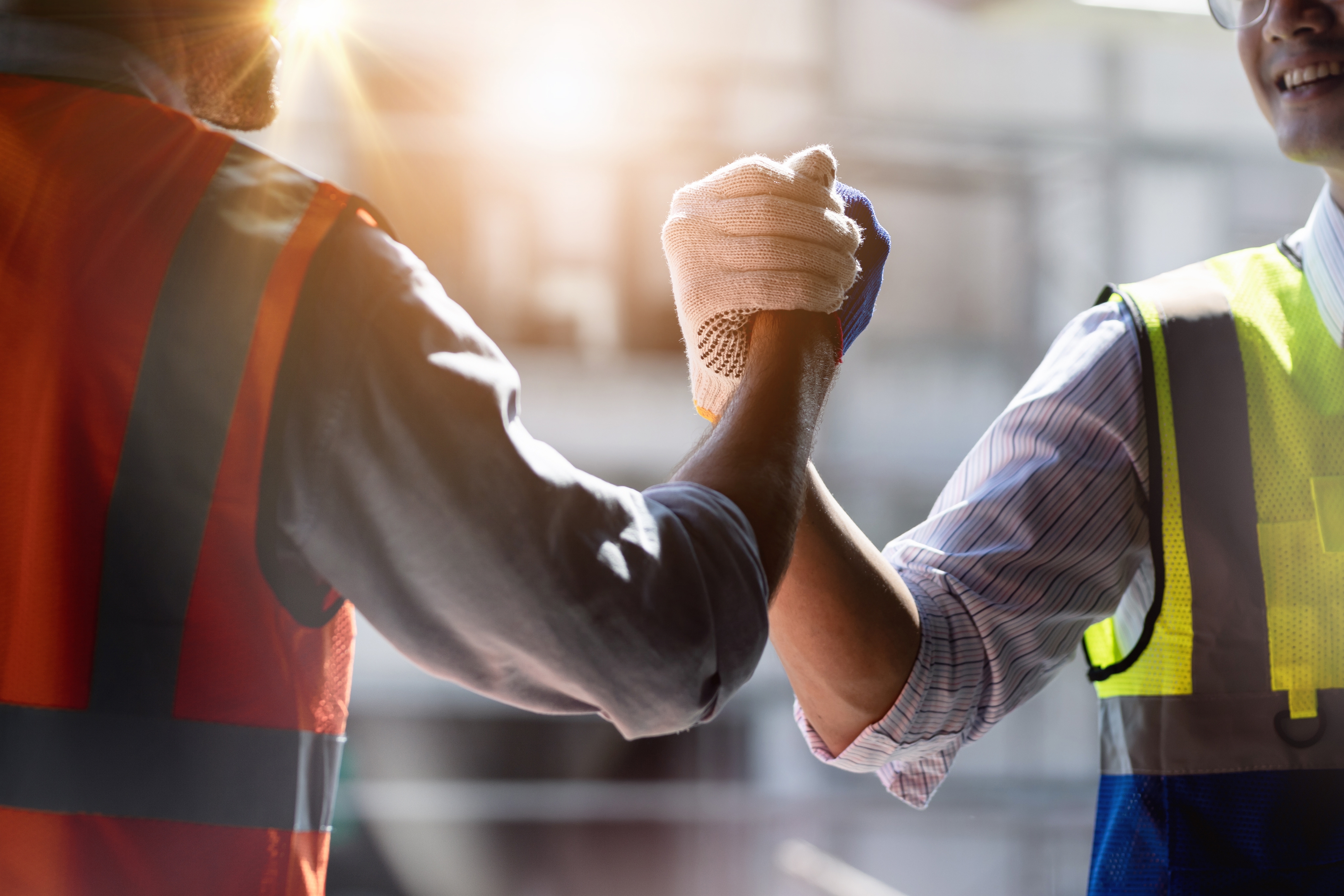 workers in safety vests clasping hands industrial background638055086954605576